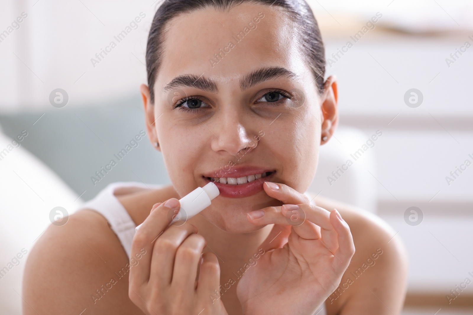 Young woman with lip balm at home Photo of Young woman with lip balm at home