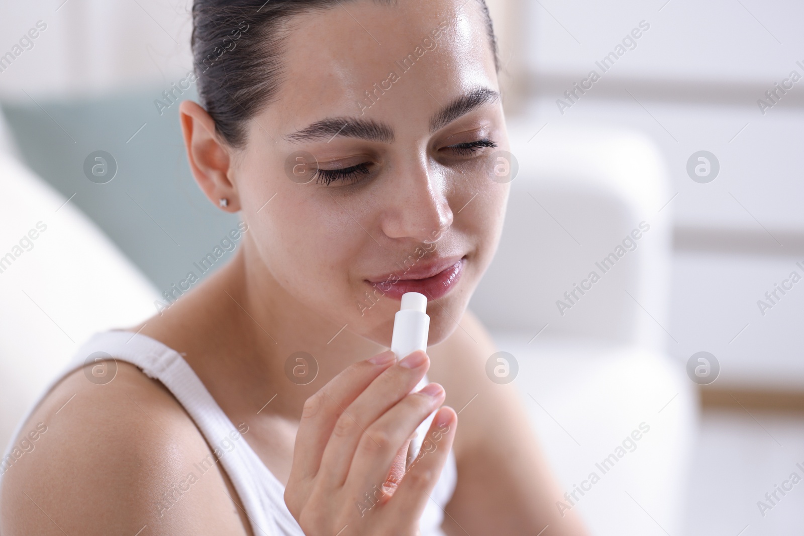 Young woman with lip balm at home Photo of Young woman with lip balm at home