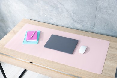 Photo of Stylish workplace with laptop and pink mousepad on wooden table indoors