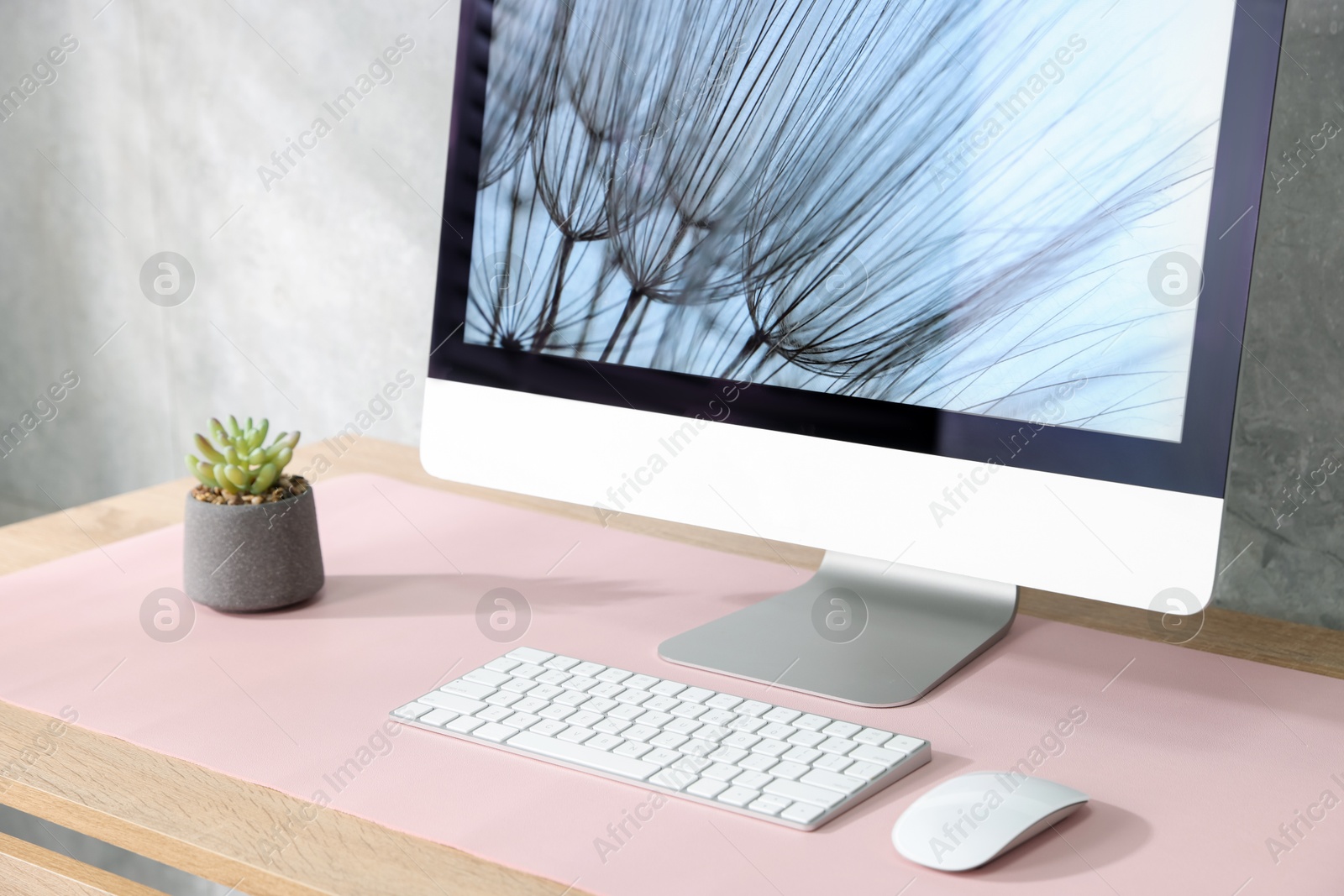 Photo of Stylish workplace with computer and pink mousepad on wooden table indoors, closeup