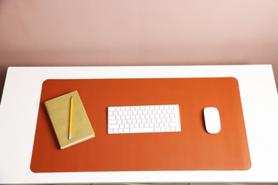 Photo of Computer keyboard, mouse, orange mousepad and notebook on white table at workplace, above view