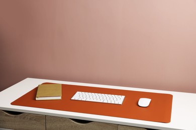Photo of Computer keyboard, mouse, orange mousepad and notebook on white table at workplace. Space for text