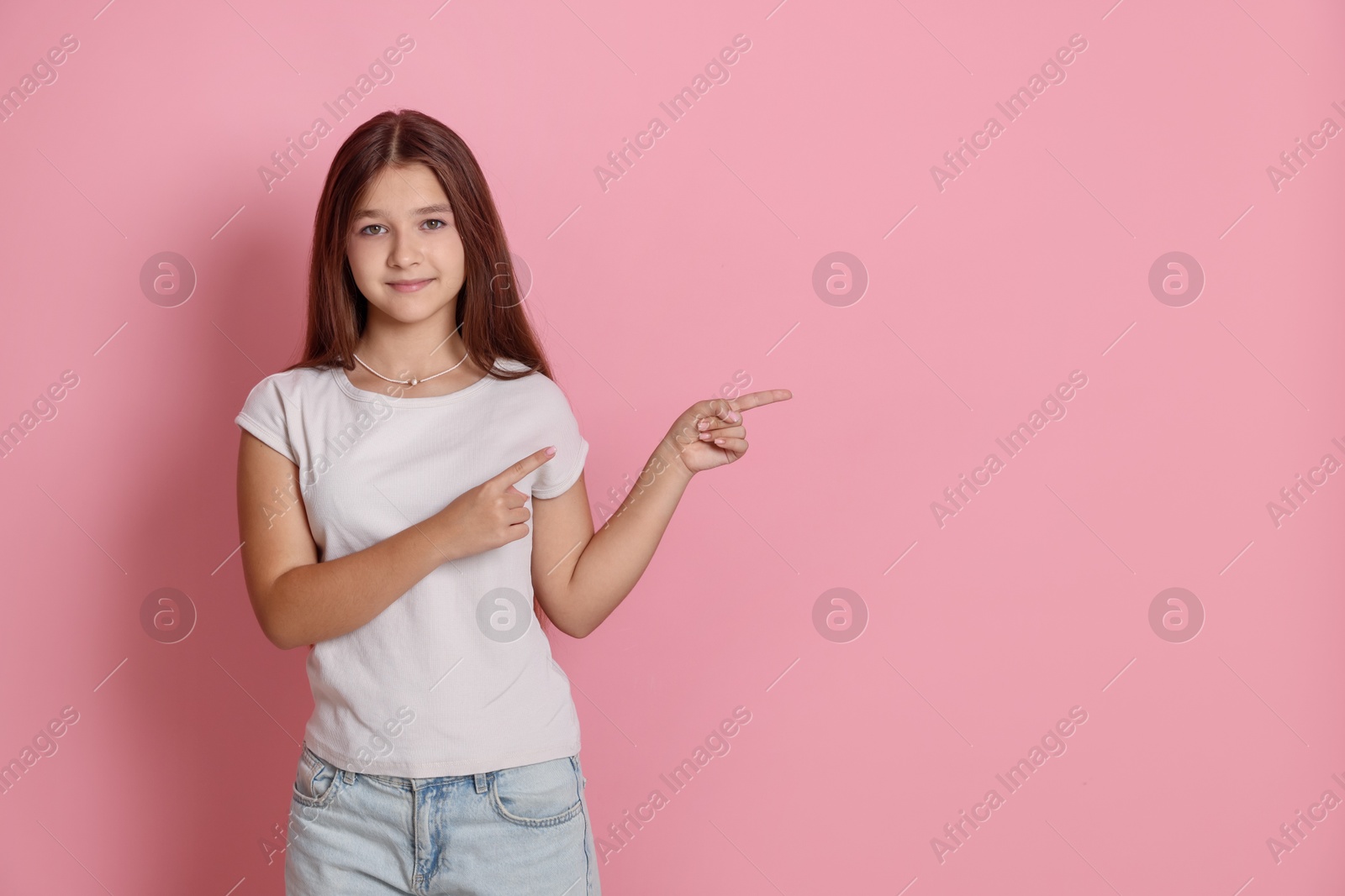 Teenage girl pointing at something on pink background, space for text Photo of Teenage girl pointing at something on pink background, space for text