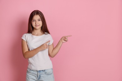 Photo of Teenage girl pointing at something on pink background, space for text
