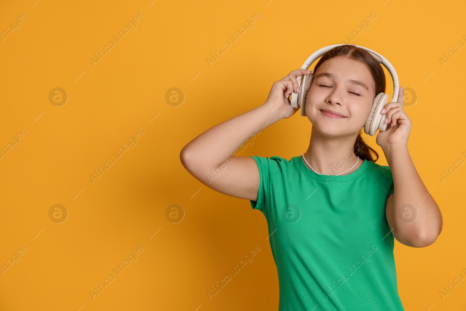 Teenage girl in headphones on orange background, space for text Photo of Teenage girl in headphones on orange background, space for text