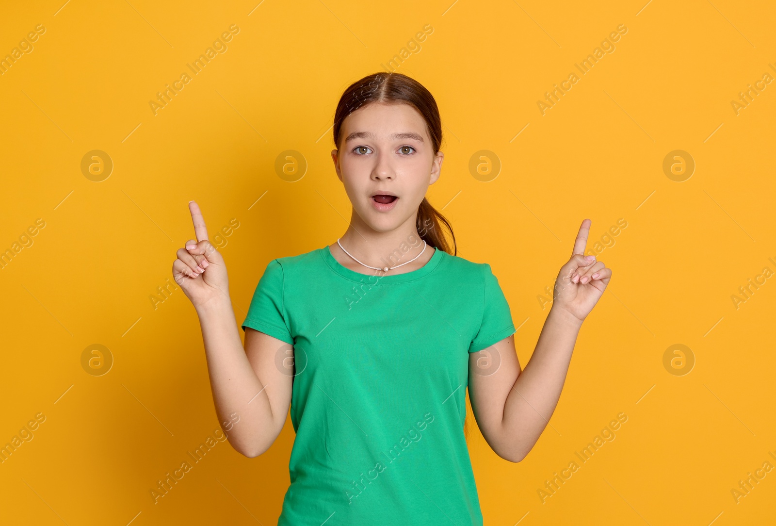 Teenage girl pointing at something on orange background Photo of Teenage girl pointing at something on orange background