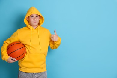 Photo of Teenage boy with basketball ball showing thumbs up on light blue background, space for text