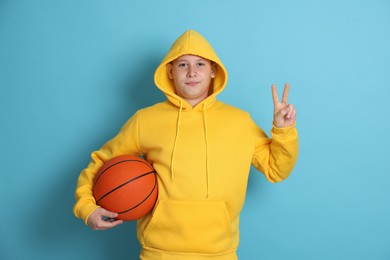 Photo of Teenage boy with basketball ball showing peace sign on light blue background
