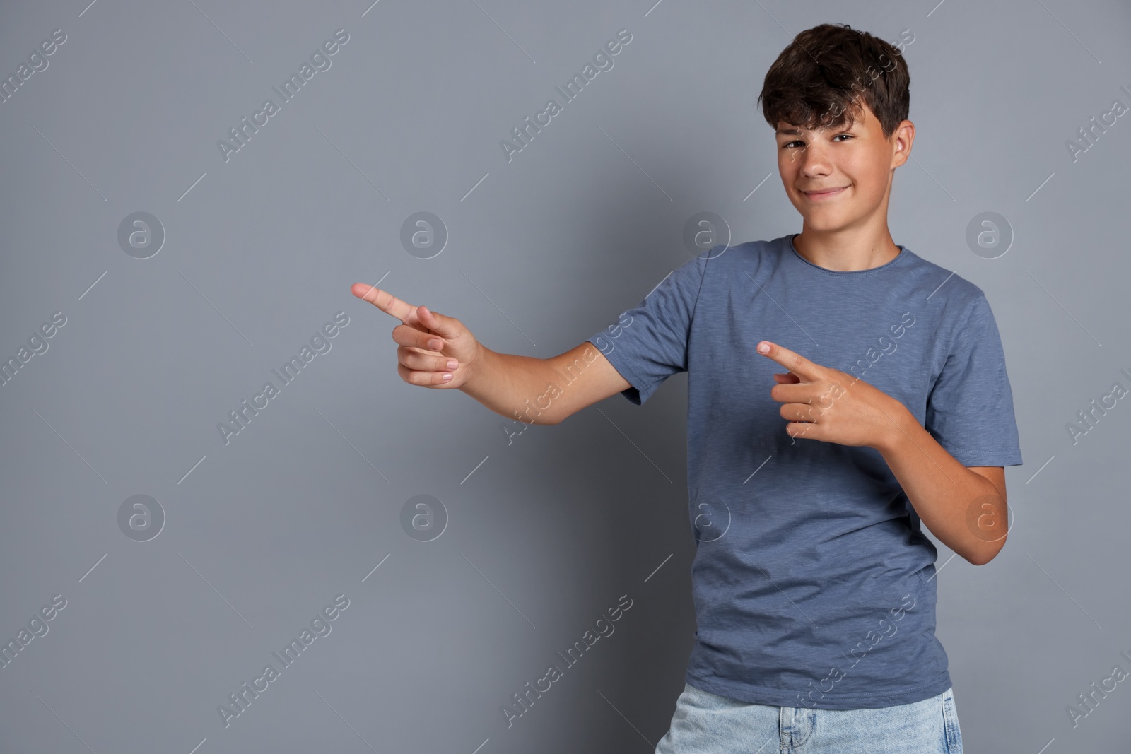 Teenage boy pointing at something on grey background, space for text Photo of Teenage boy pointing at something on grey background, space for text