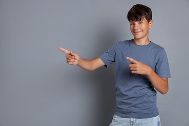 Photo of Teenage boy pointing at something on grey background, space for text