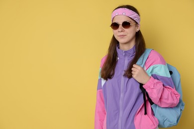 Photo of Teenage girl in sunglasses with backpack on yellow background, space for text