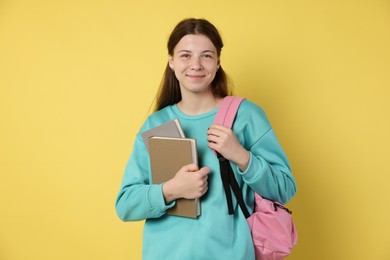 Photo of Teenage girl with backpack and books on yellow background