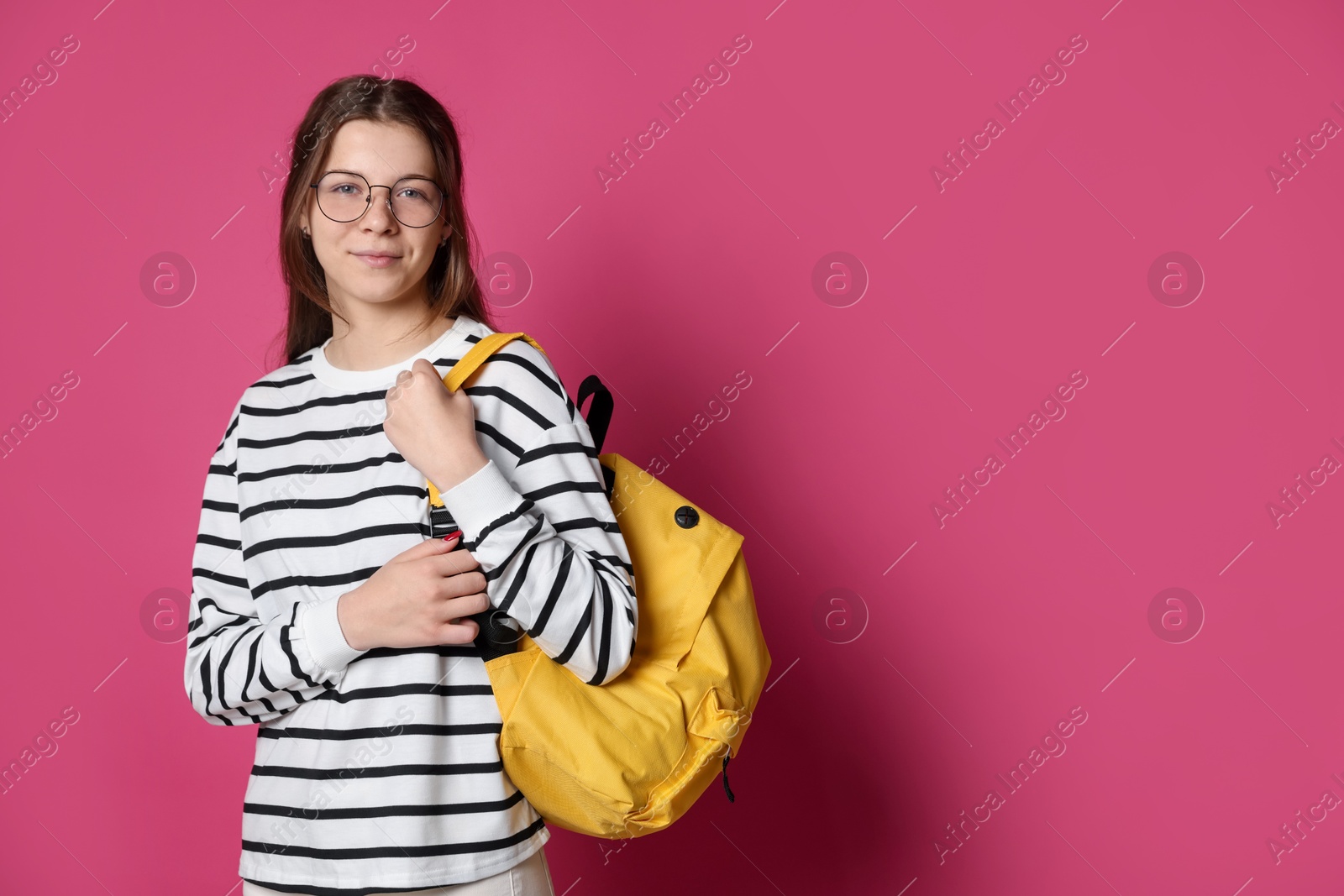Teenage girl in glasses with backpack on crimson background, space for text Photo of Teenage girl in glasses with backpack on crimson background, space for text