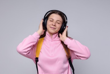 Photo of Teenage girl in headphones with backpack on light grey background