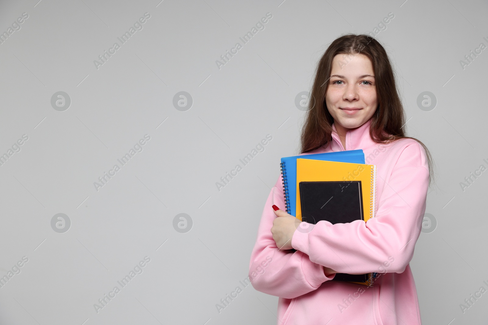 Teenage girl with notebooks on light grey background, space for text Photo of Teenage girl with notebooks on light grey background, space for text