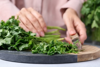 Photo of Woman cutting fresh green cilantro at light table, closeup