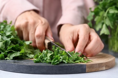 Photo of Woman cutting fresh green cilantro at light table, closeup