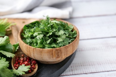 Photo of Fresh green cilantro and peppercorns on white wooden table, closeup. Space for text