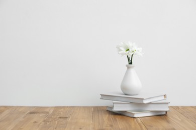 Photo of Chrysanthemum flowers in vase and books on wooden table near white wall indoors, space for text