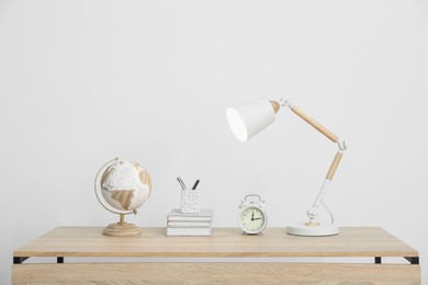 Photo of Lamp, books, stationery, alarm clock and globe on wooden table near white wall indoors