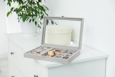 Photo of Jewelry box with many different accessories and green houseplant on white cabinet indoors