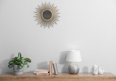 Photo of Lamp, books, vases and green houseplant on wooden table near white wall indoors