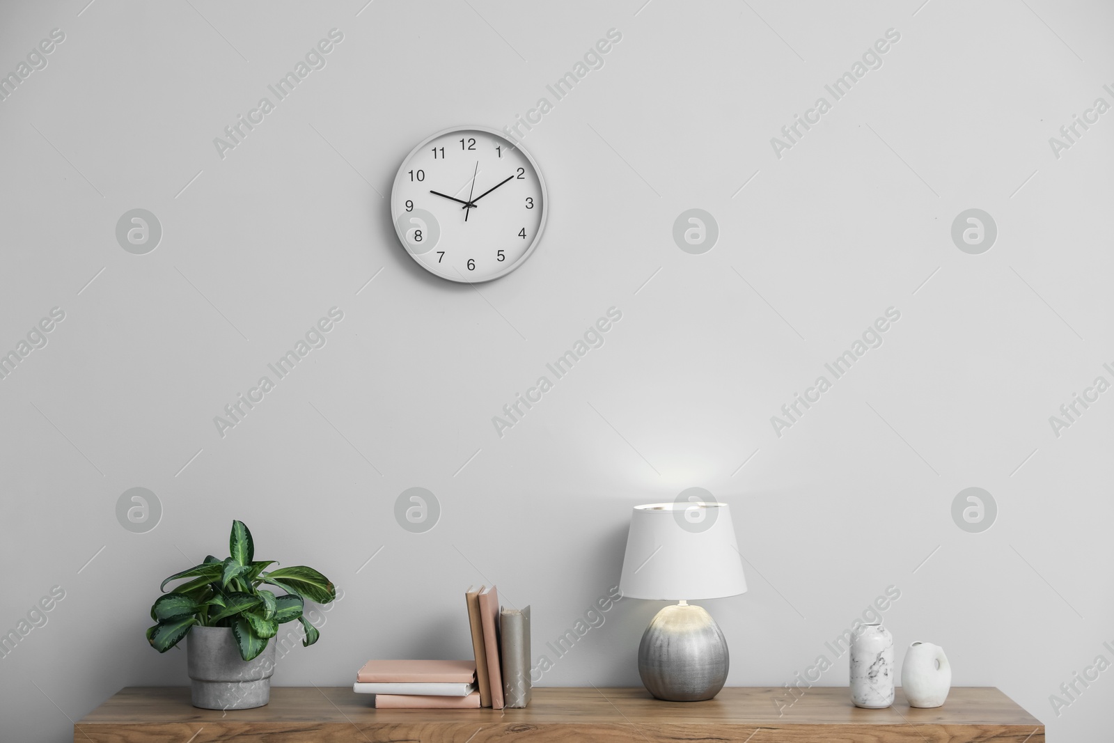 Lamp, books, vases and green houseplant on wooden table near white wall indoors Photo of Lamp, books, vases and green houseplant on wooden table near white wall indoors