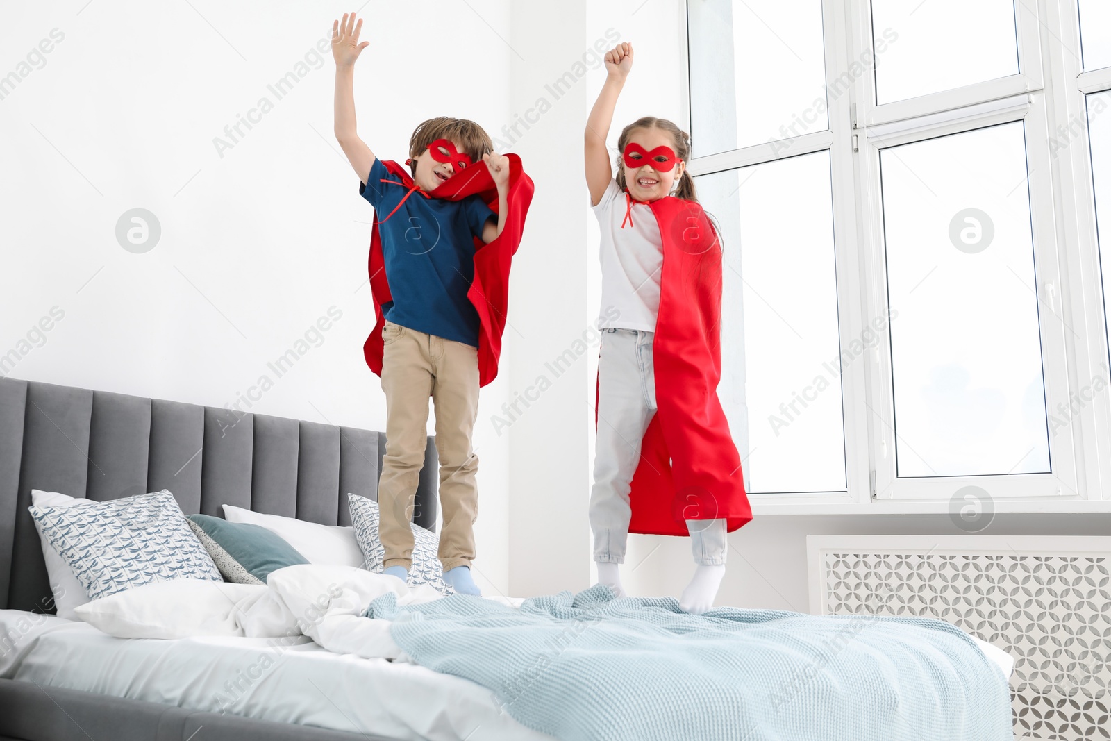 Photo of Children in superhero costumes jumping on bed at home