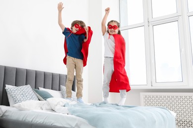 Photo of Children in superhero costumes jumping on bed at home
