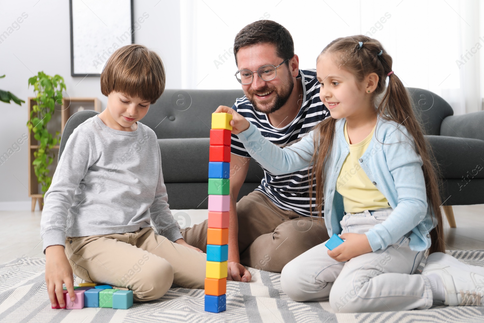 Photo of Father and his children playing with colorful cubes on floor at home