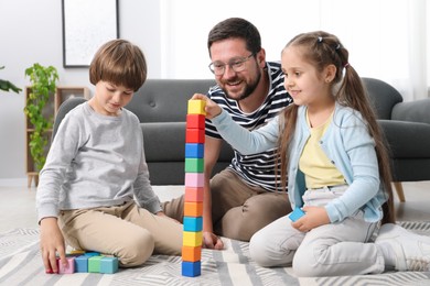 Photo of Father and his children playing with colorful cubes on floor at home