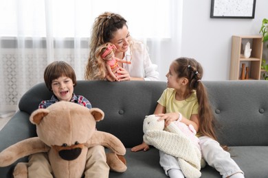 Photo of Children and their mother playing with different toys on sofa at home