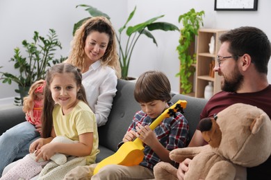 Photo of Children and their parents playing with different toys on sofa at home
