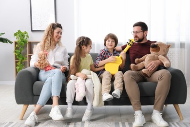 Photo of Children and their parents playing with different toys on sofa at home