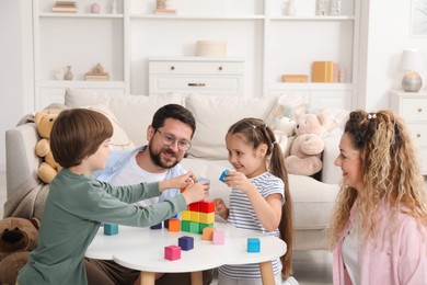 Photo of Children and their parents building tower with colorful cubes at white table indoors