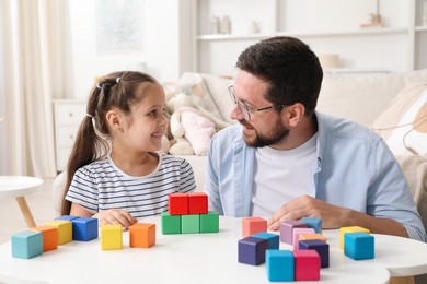 Photo of Father and his daughter playing with colorful cubes at white table indoors