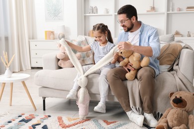 Photo of Father and his daughter playing with stuffed animals on sofa at home