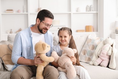 Photo of Father and his daughter playing with teddy bears on sofa at home