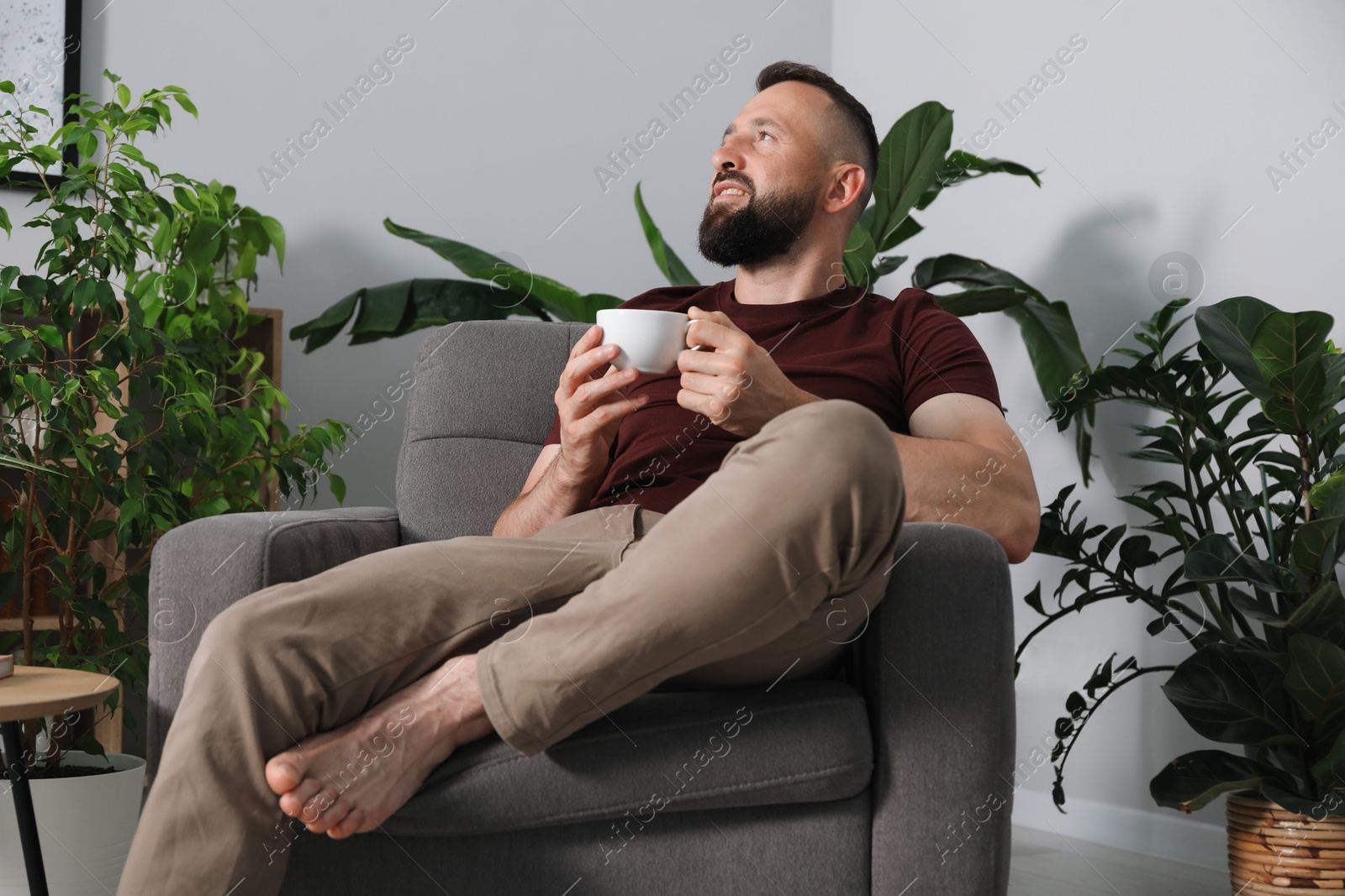 Photo of Harmony. Man with cup of drink in armchair at home