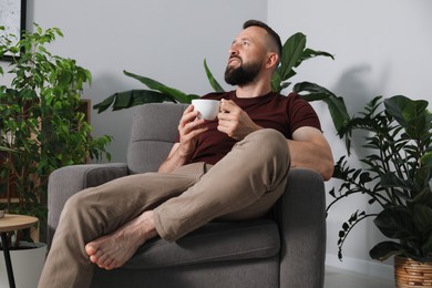 Photo of Harmony. Man with cup of drink in armchair at home