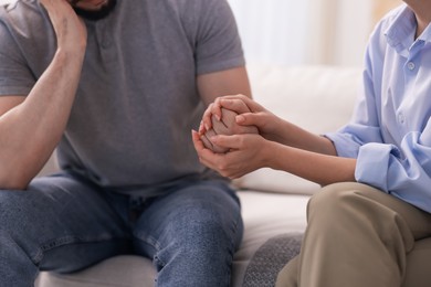 Photo of Psychologist supporting patient during therapy session on sofa in office, closeup