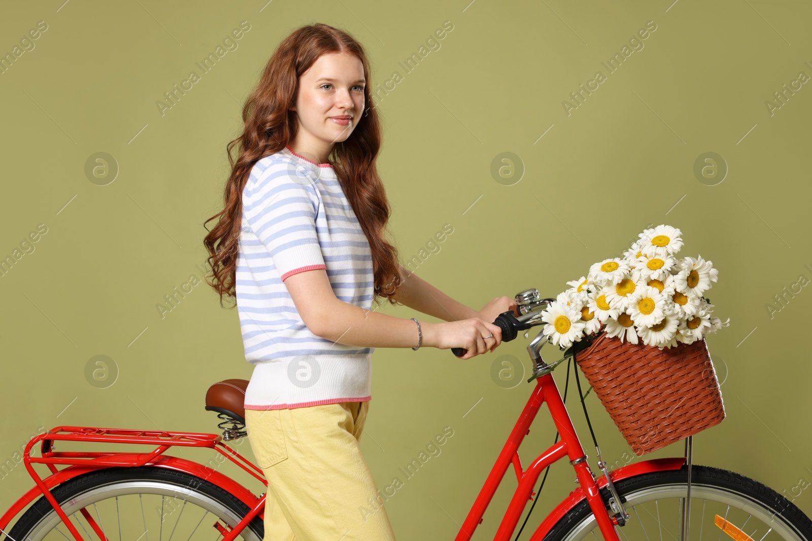 Beautiful teenage girl and bicycle with basket of flowers against green background Photo of Beautiful teenage girl and bicycle with basket of flowers against green background