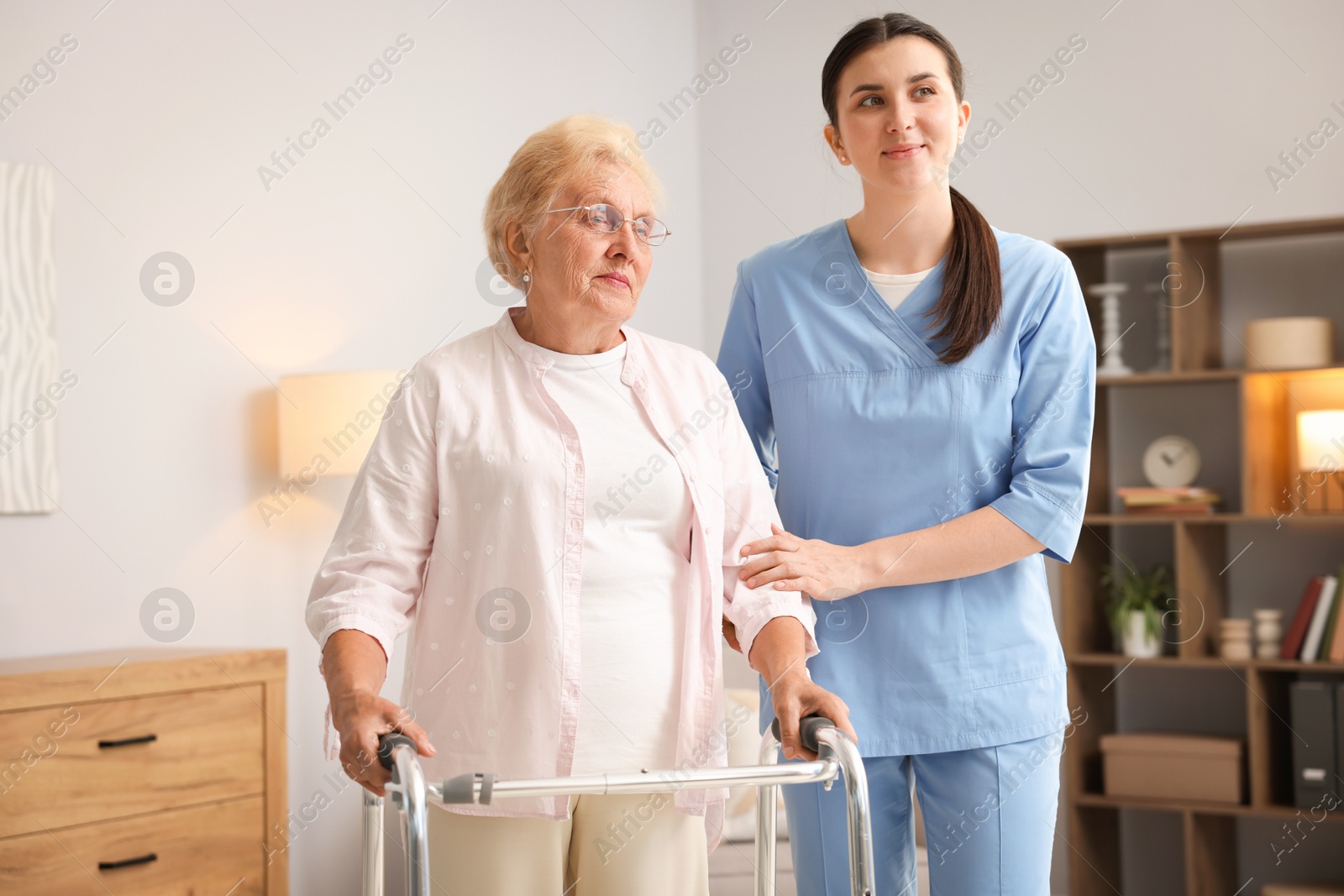 Nurse assisting senior woman with walking frame indoors. Home health care service Photo of Nurse assisting senior woman with walking frame indoors. Home health care service