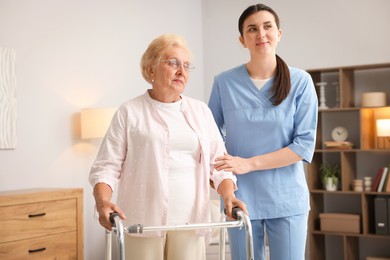 Photo of Nurse assisting senior woman with walking frame indoors. Home health care service