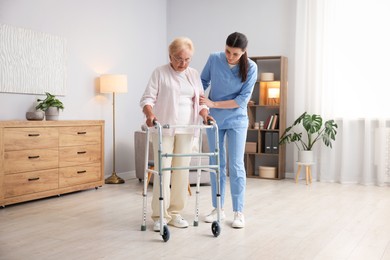 Photo of Nurse assisting senior woman with walking frame indoors. Home health care service