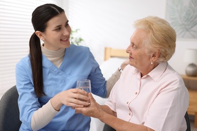 Photo of Nurse giving glass of water to senior woman indoors. Home health care service