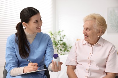 Photo of Nurse giving pills to senior woman indoors. Home health care service
