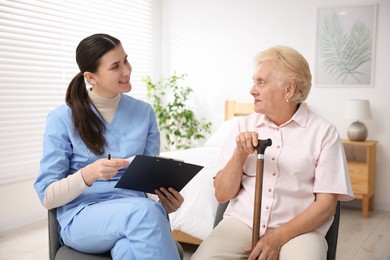 Photo of Nurse with clipboard examining senior woman indoors. Home health care service
