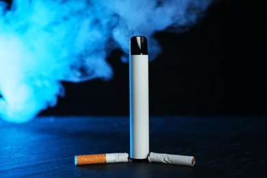 Photo of Electronic smoking device and broken cigarette on black table in blue light