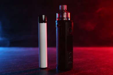 Photo of Electronic smoking devices on black table in red light